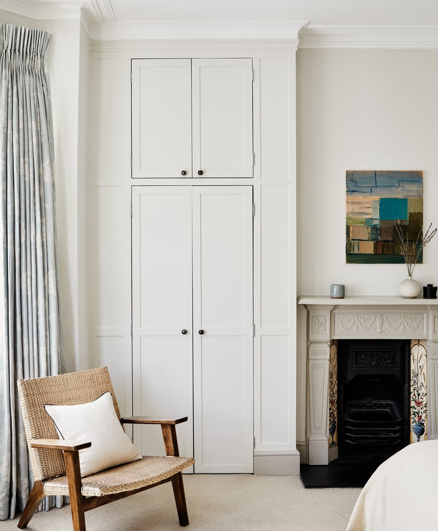 White cabinet with a wooden chair and abstract painting in a room.