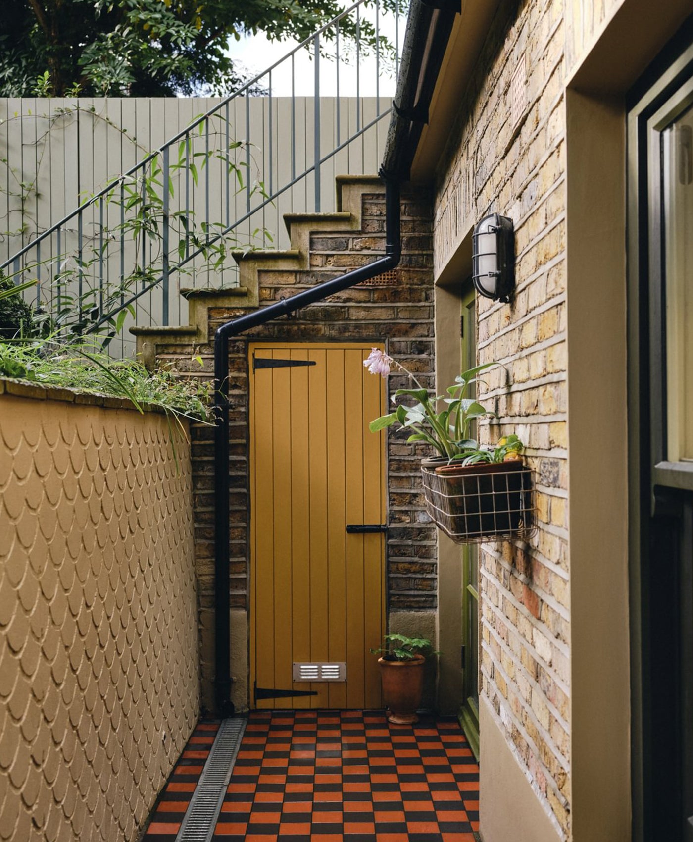 Ochre yellow door with plants on a checkered patio area