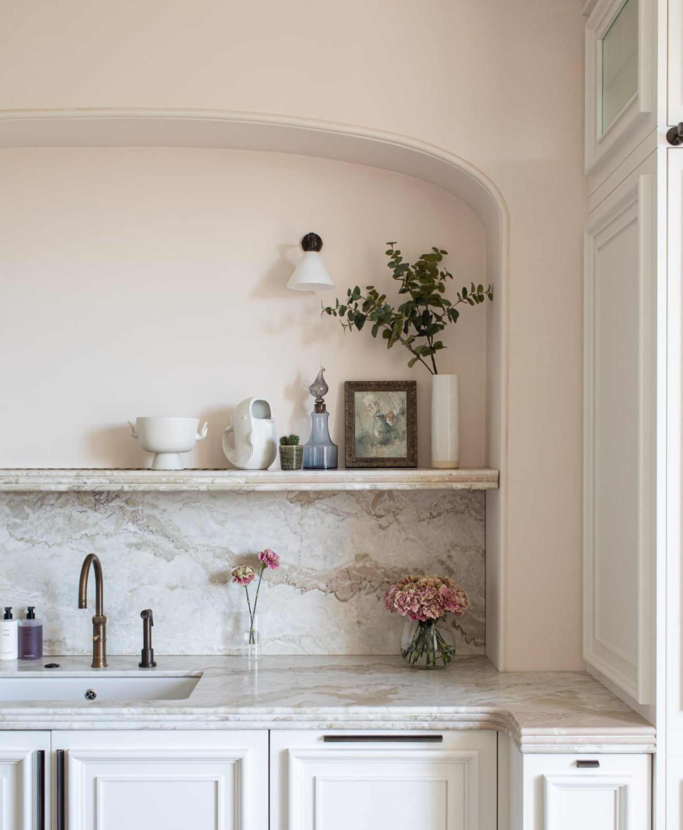 Modern pale pink kitchen with marble countertop, sink, and decorative elements.