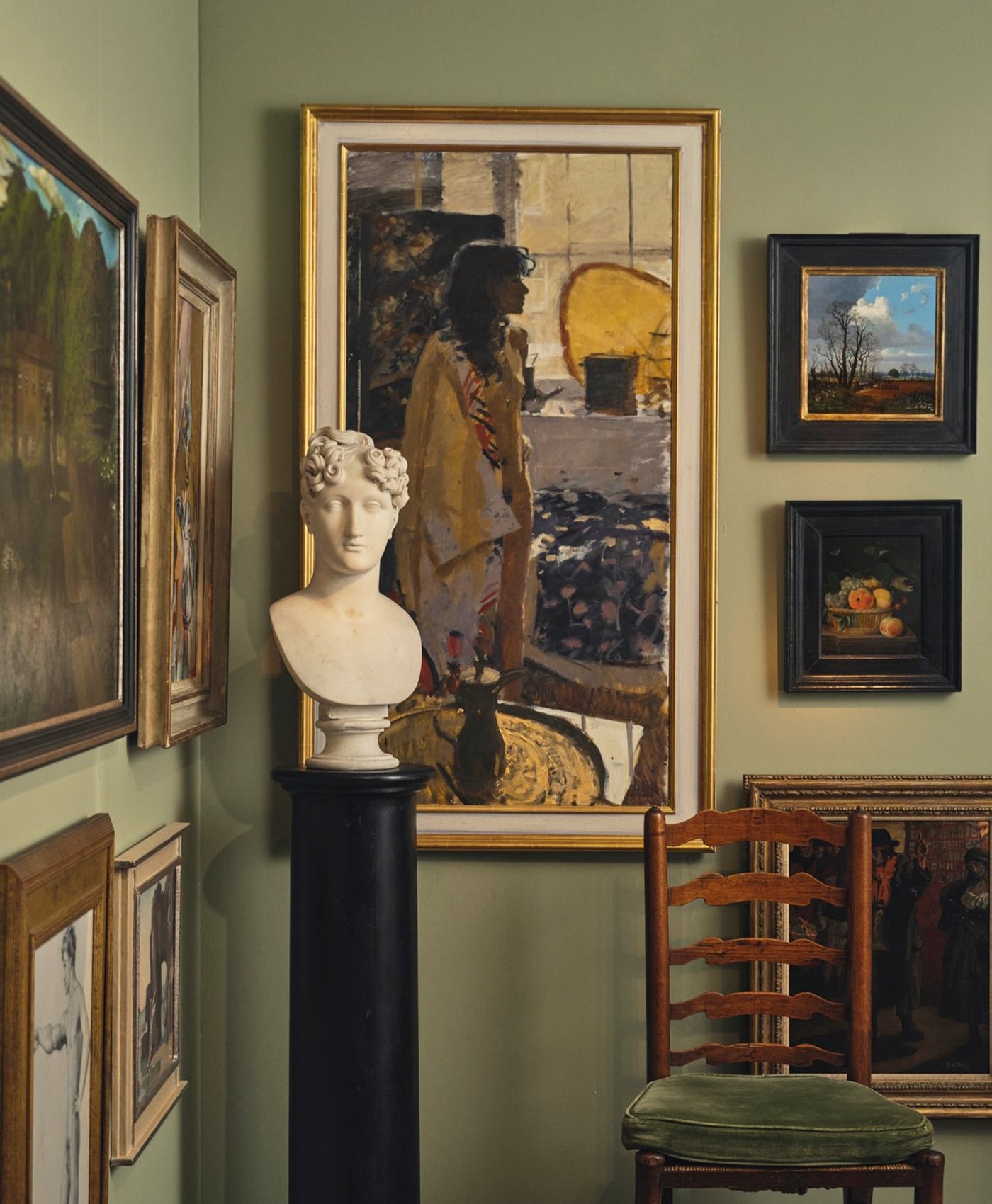 Art gallery with framed paintings on a green wall, including a bust and a chair.