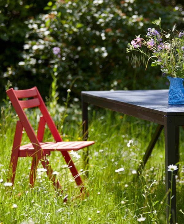 Red chair and black table in a grassy outdoor setting with flowers.