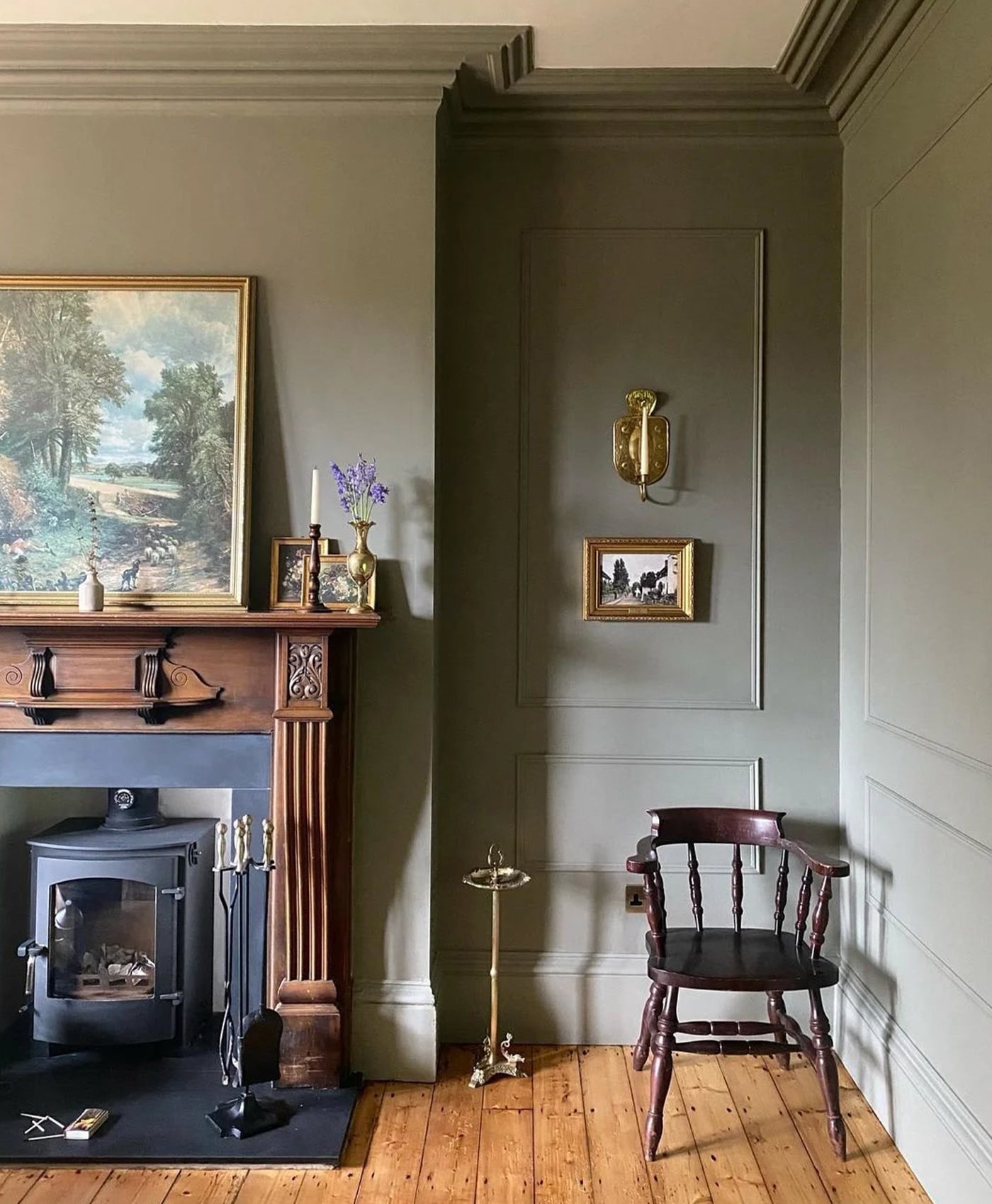 Victorian room colour drenched in green grey paint with a fireplace, wooden chair, and wall art.
