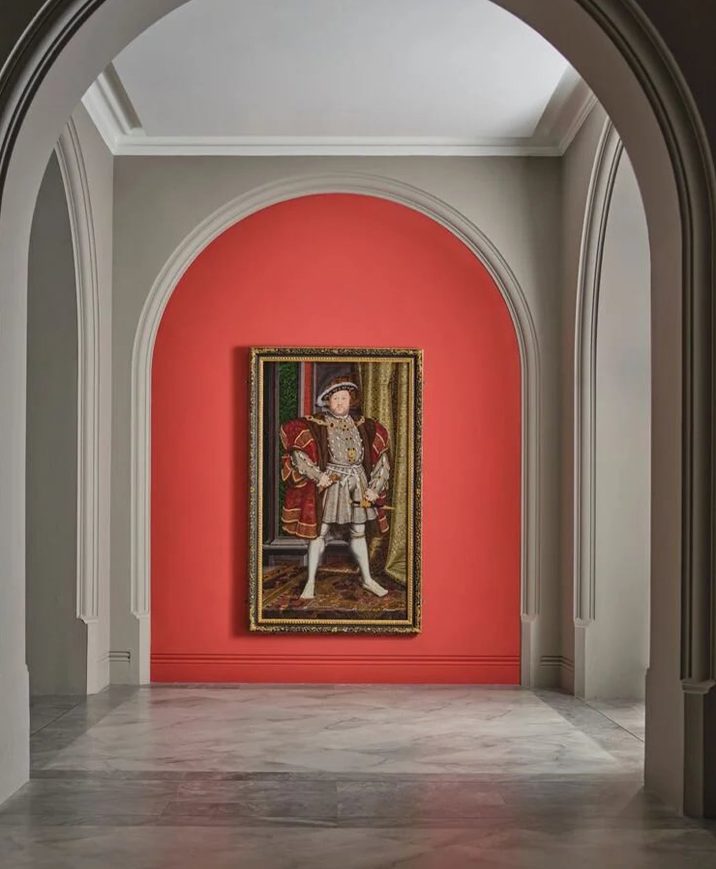 Portrait of King Henry VIII on a red wall in an elegant hallway.