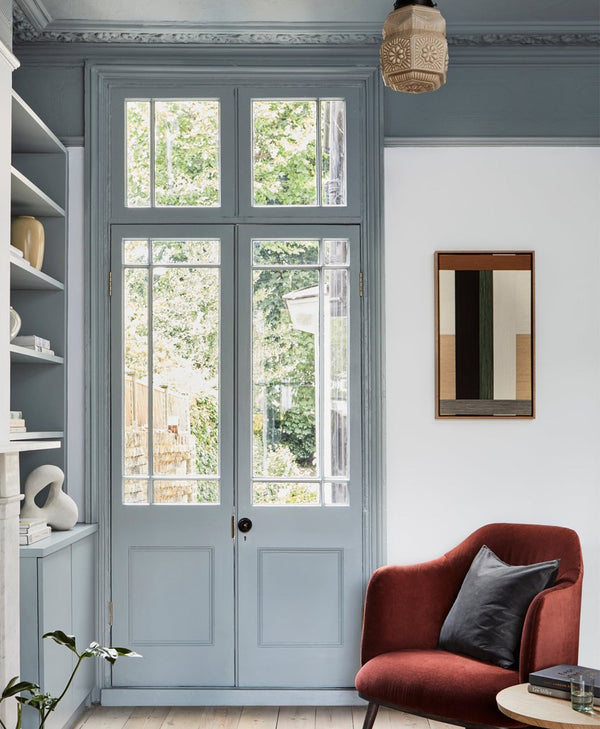 Victorian interior with a red armchair, dusty blue shelves, light blue walls and a large window.