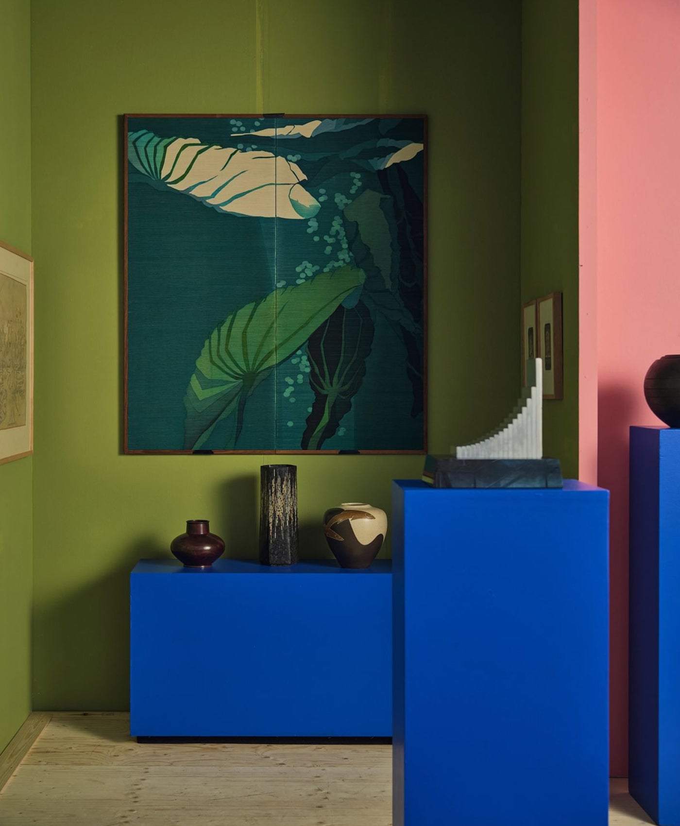 Room interior with an olive green wall, blue cabinet, and decorative items.