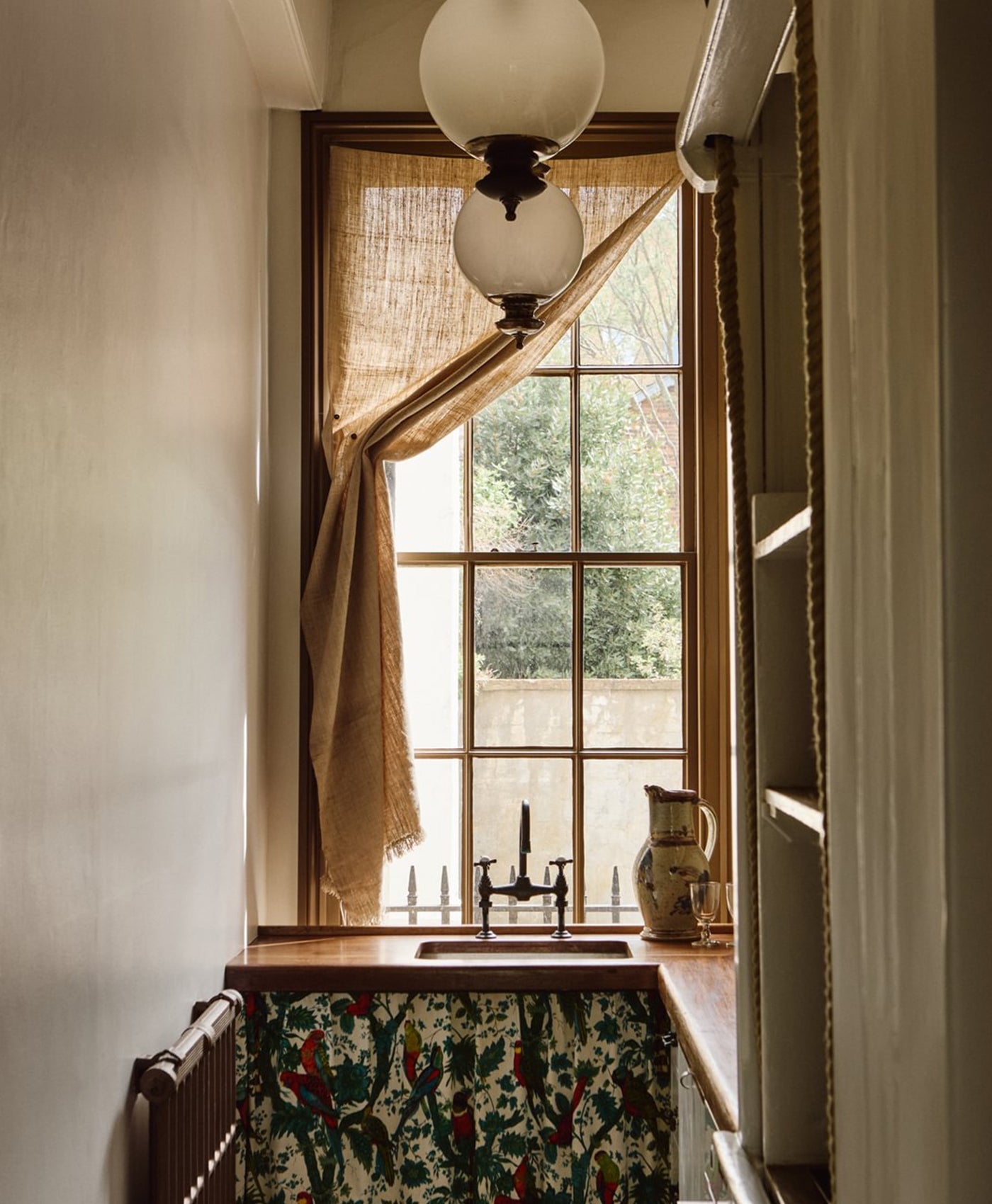 Window of utility room with curtains and a light fixture, showing a view of trees outside. Painted in warm neutral colour.