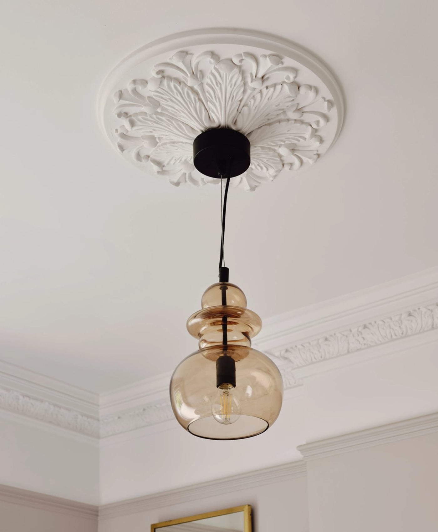 Period ceiling rose with pendant light with glass shade hanging from off-white pink painted ceiling