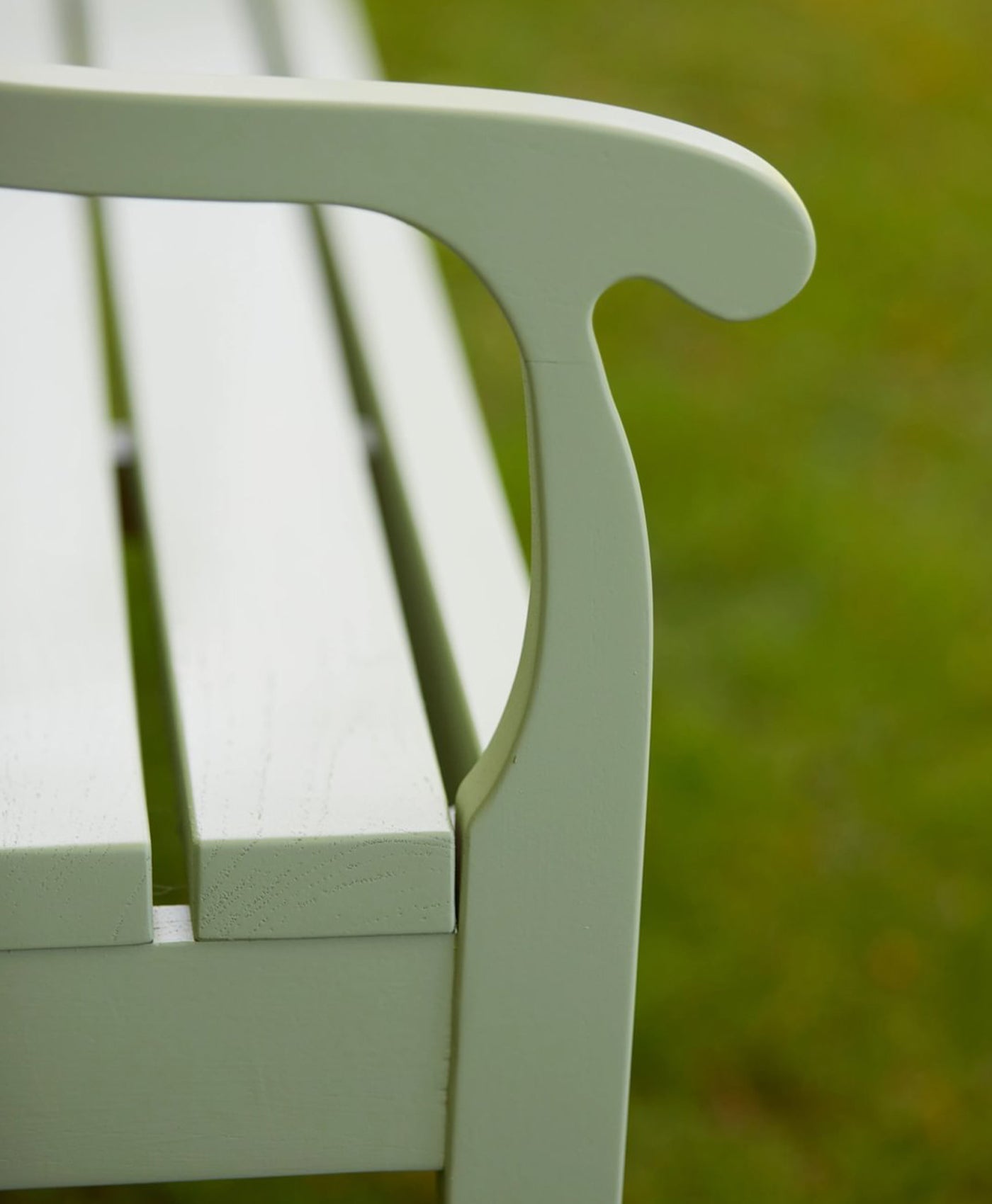 Close-up of a light green bench with a blurred grass background