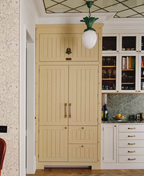 butter yellow pantry cabinet with gold handles in a kitchen setting