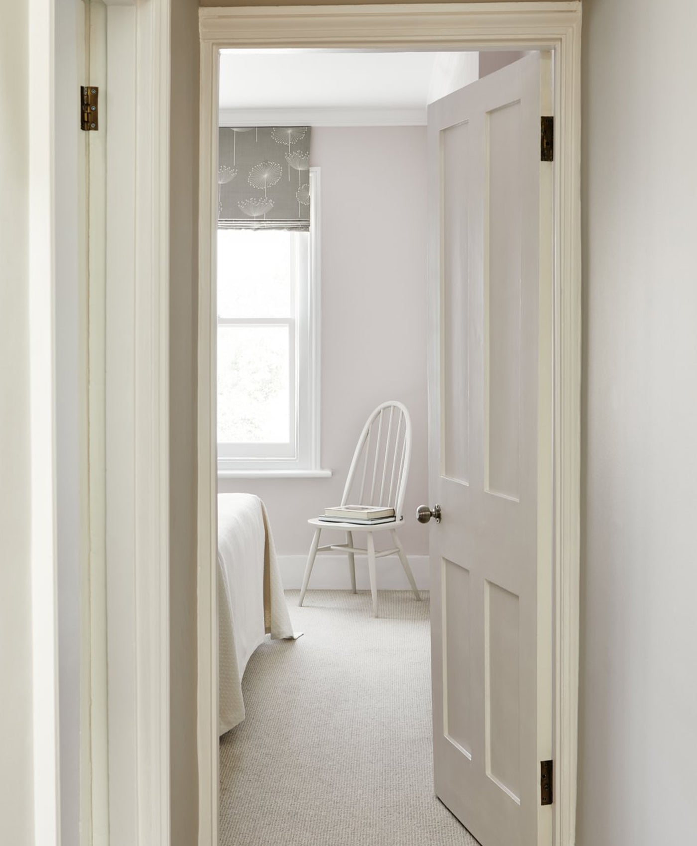 Open door leading into a light neutral coloured bedroom with a bed and chair.