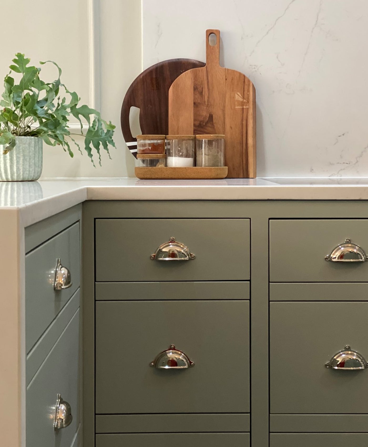Kitchen cabinet with grey green drawers and wooden cutting boards on a countertop.