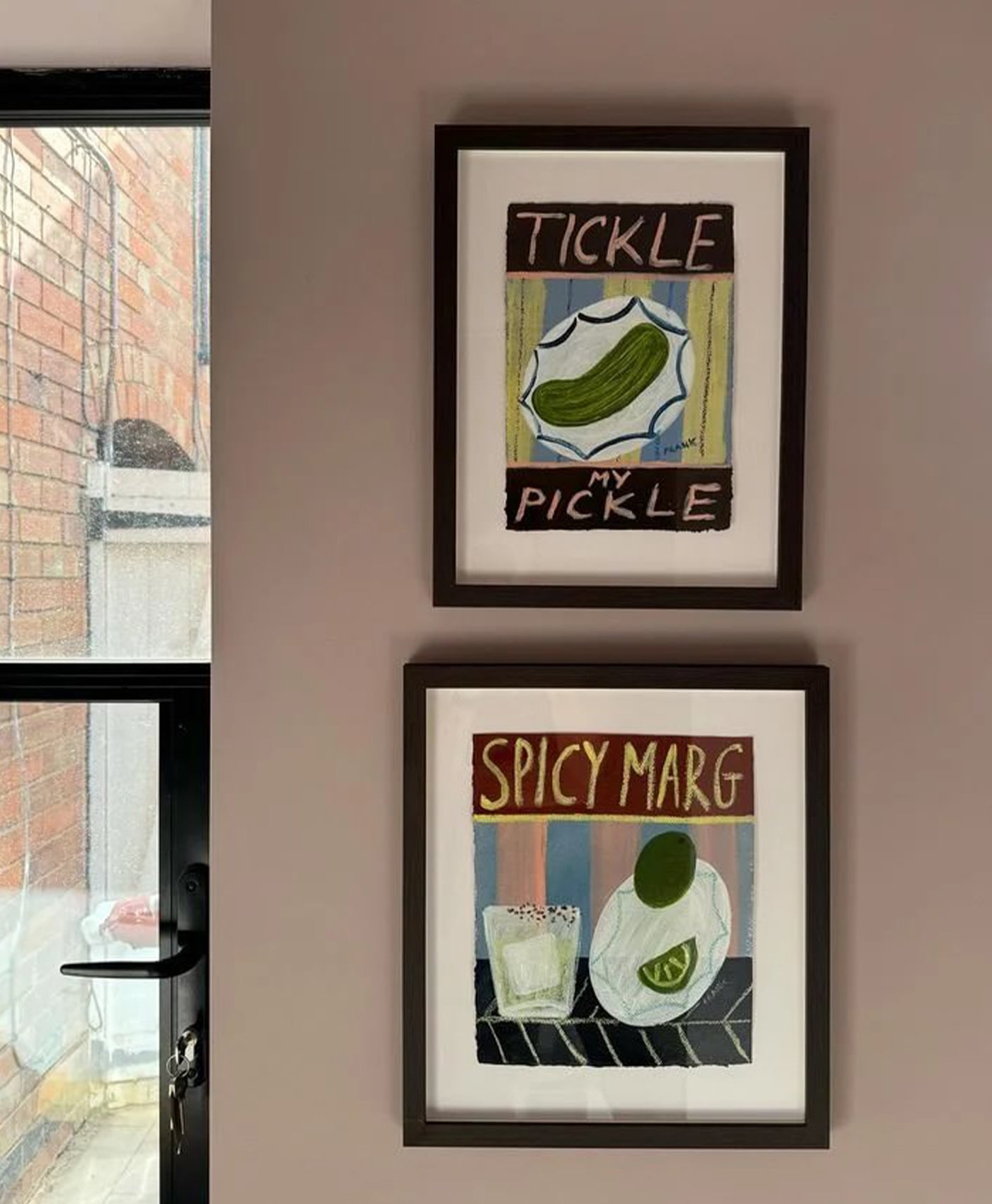 Two framed prints on a dusty wall, with a brick wall and window in the background.