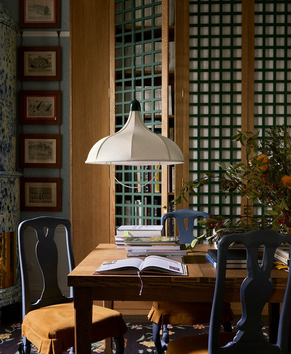 Dining area with wooden table, navy blue painted chairs, and a lamp in a room with decorative green lattice detail on the walls.