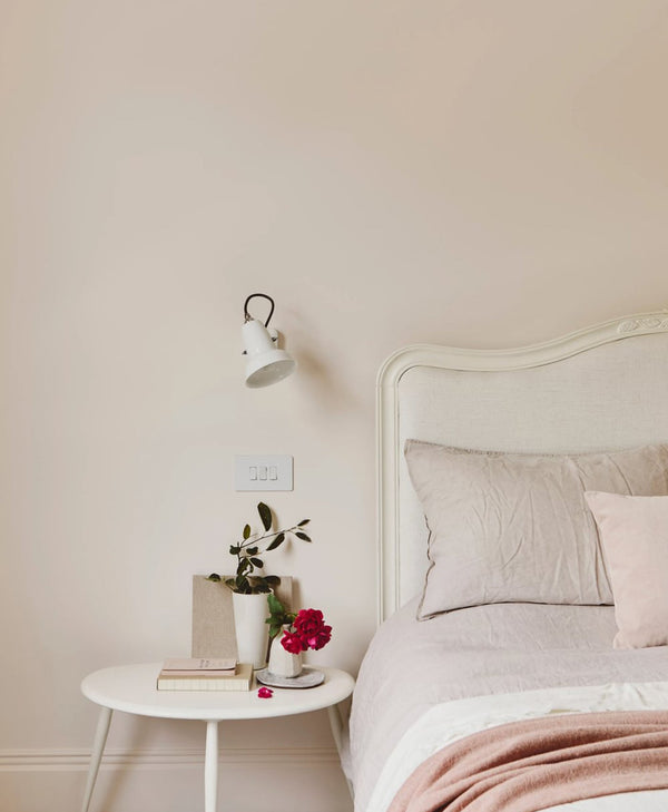 Pale pink bedroom with a bed, nightstand, and wall lamp.