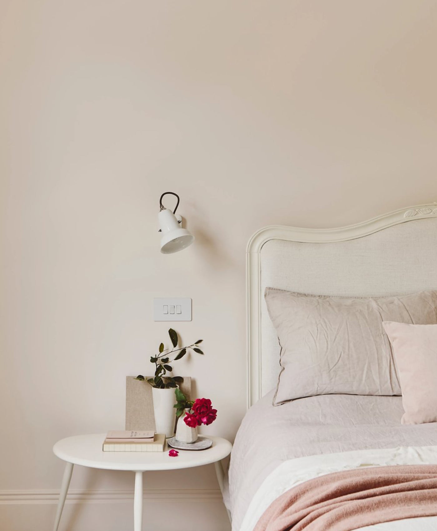 Pale pink bedroom with a bed, nightstand, and wall lamp.