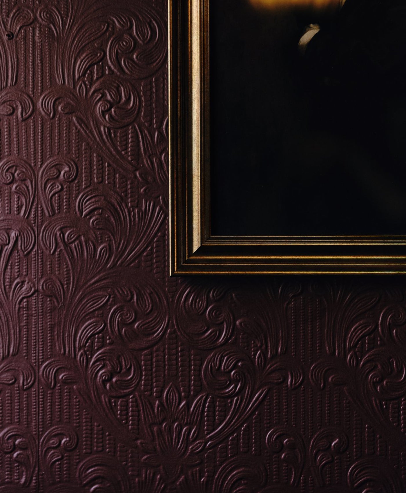 Decorative embossed wallpaper painted in a burgundy red with a gold frame corner