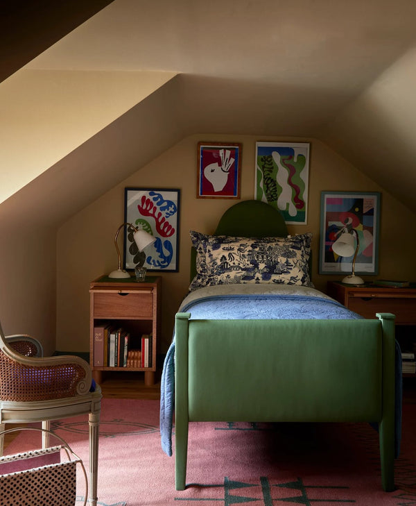 Children's bedroom in butter yellow with green bed, colourful artwork on the wall, and wooden furniture.