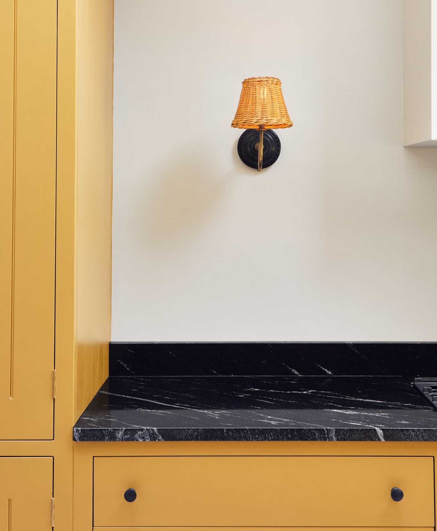 Yellow cabinet with black marble countertop and lamp mounted on stone white wall.