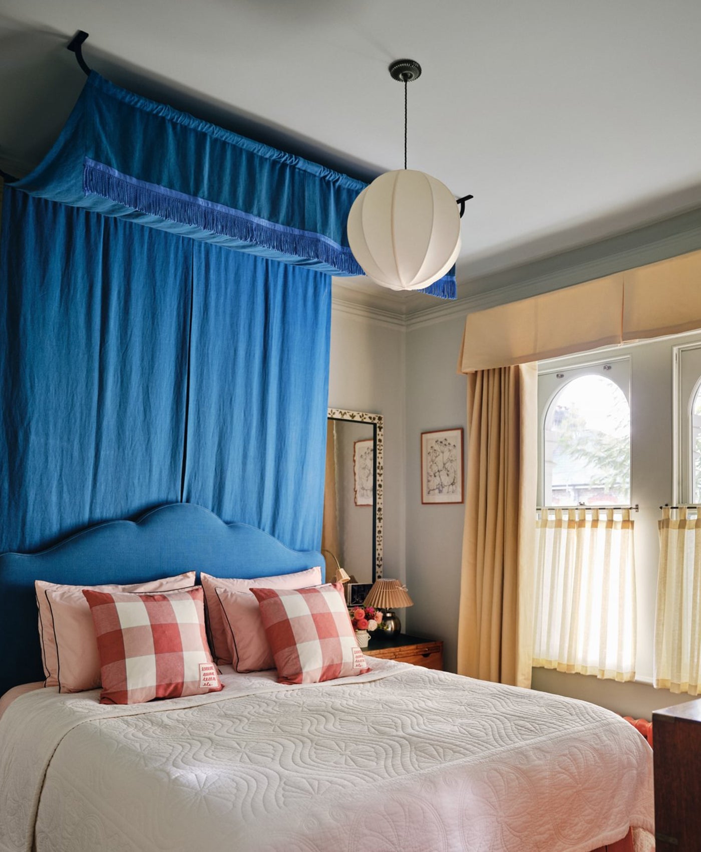 Pale green bedroom with blue canopy, pink checkered pillows, and a lamp hanging above.