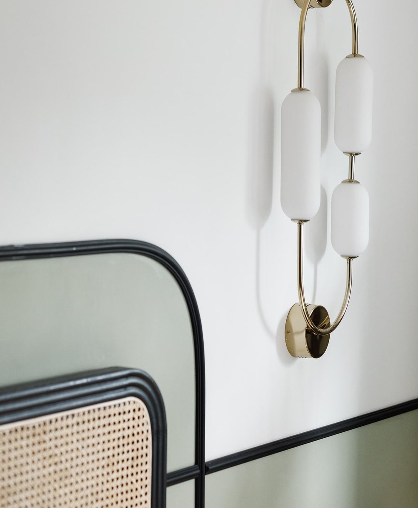 Modern wall sconce with white glass shades and gold accents on a white wall with pale green base and black trim