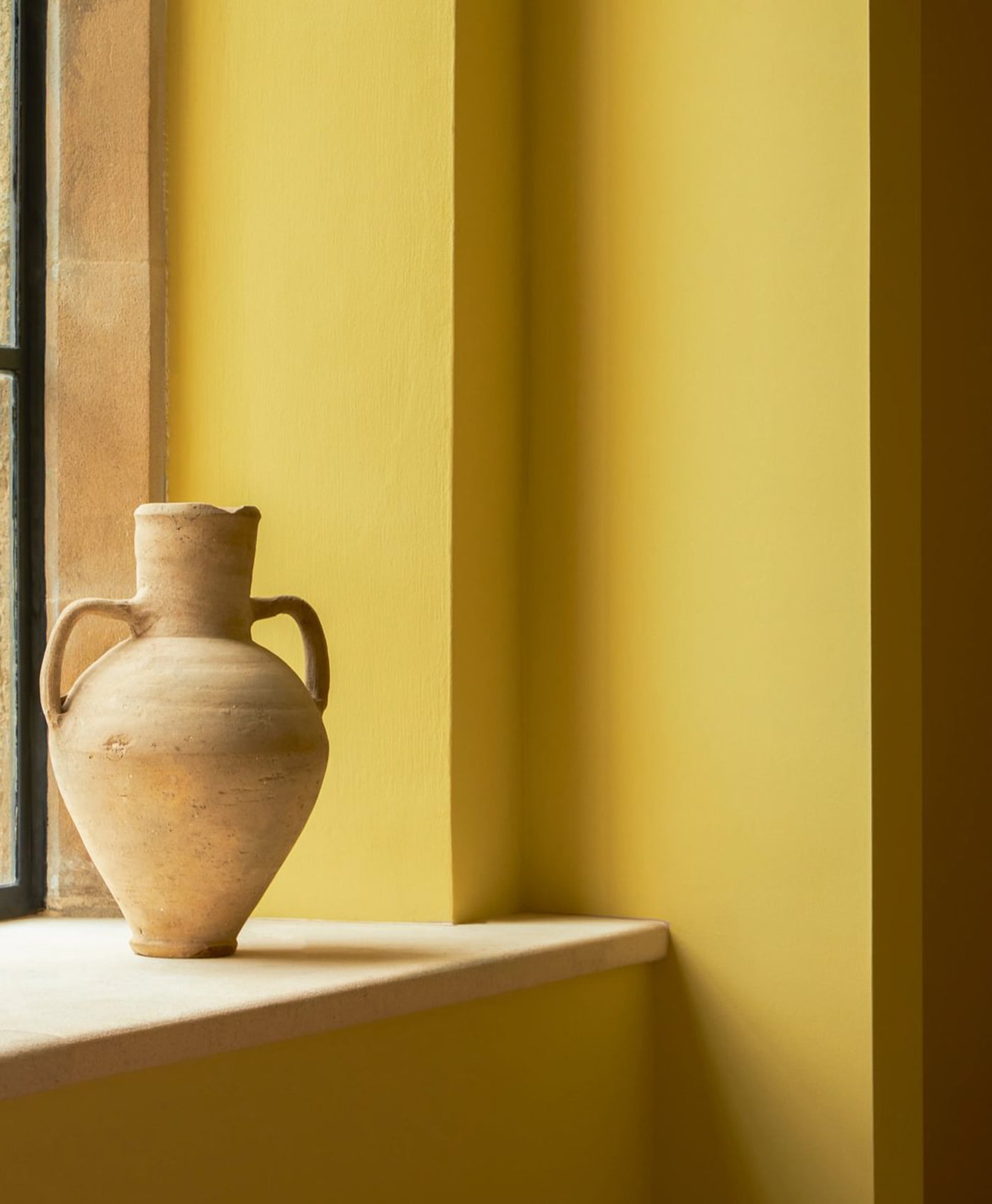 Terracotta vase on a windowsill with a yellow wall in the background