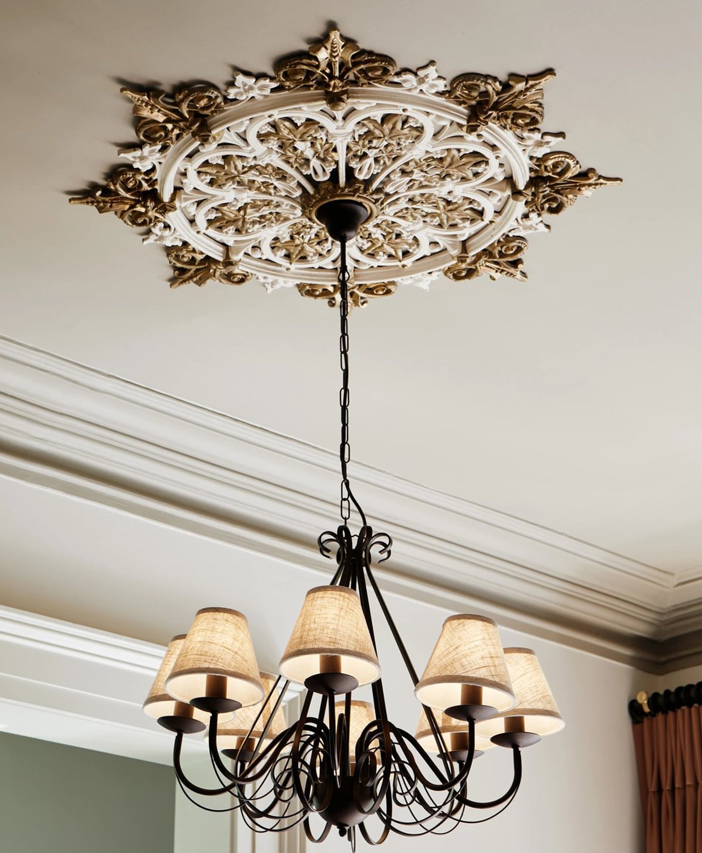 Decorative chandelier hanging from a ornate ceiling rose in neutral painted room.