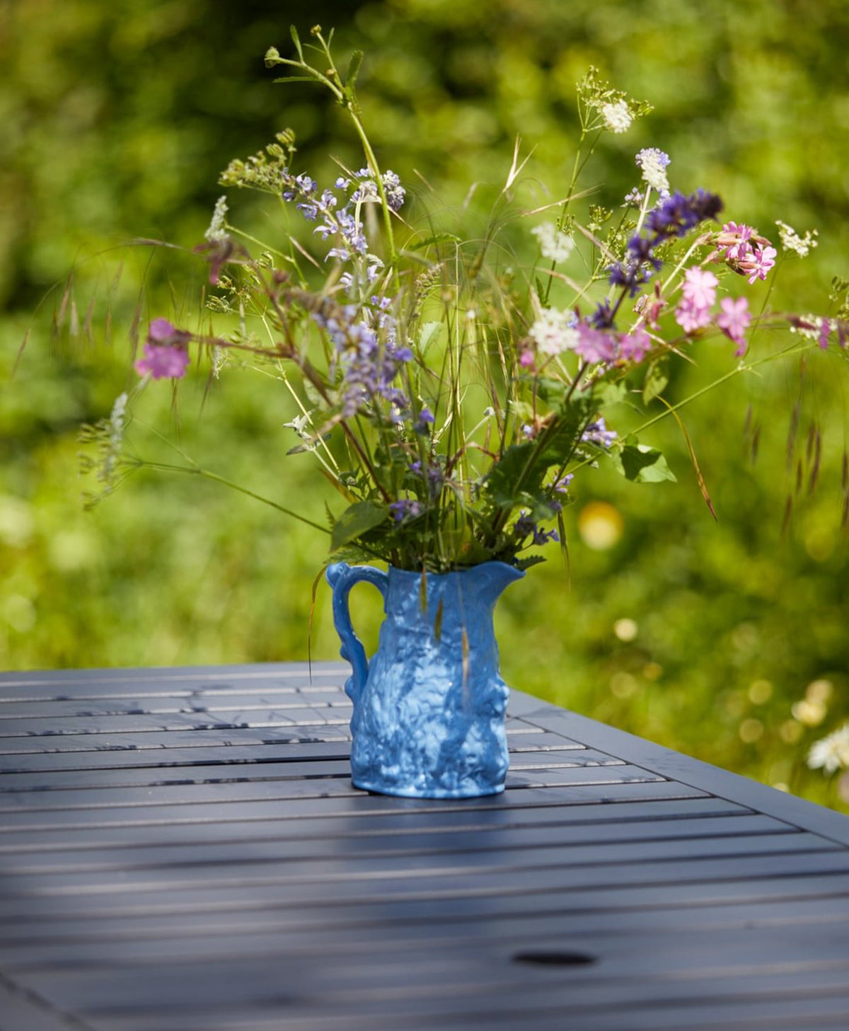 Blue ceramic vase with wildflowers on a wooden table painted in deep blue outdoors