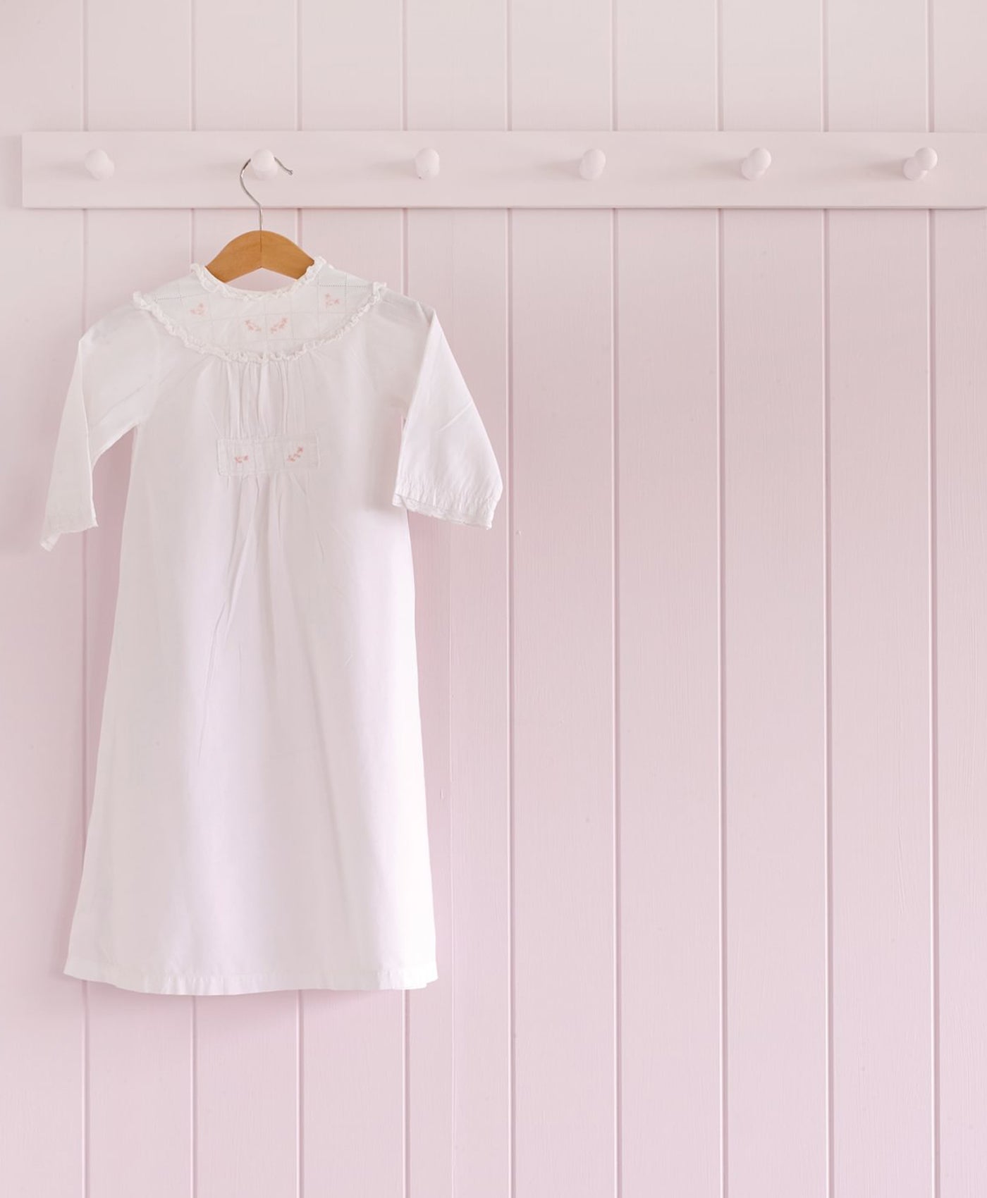 White dress hanging on a wooden hanger against a light pink wooden panel background