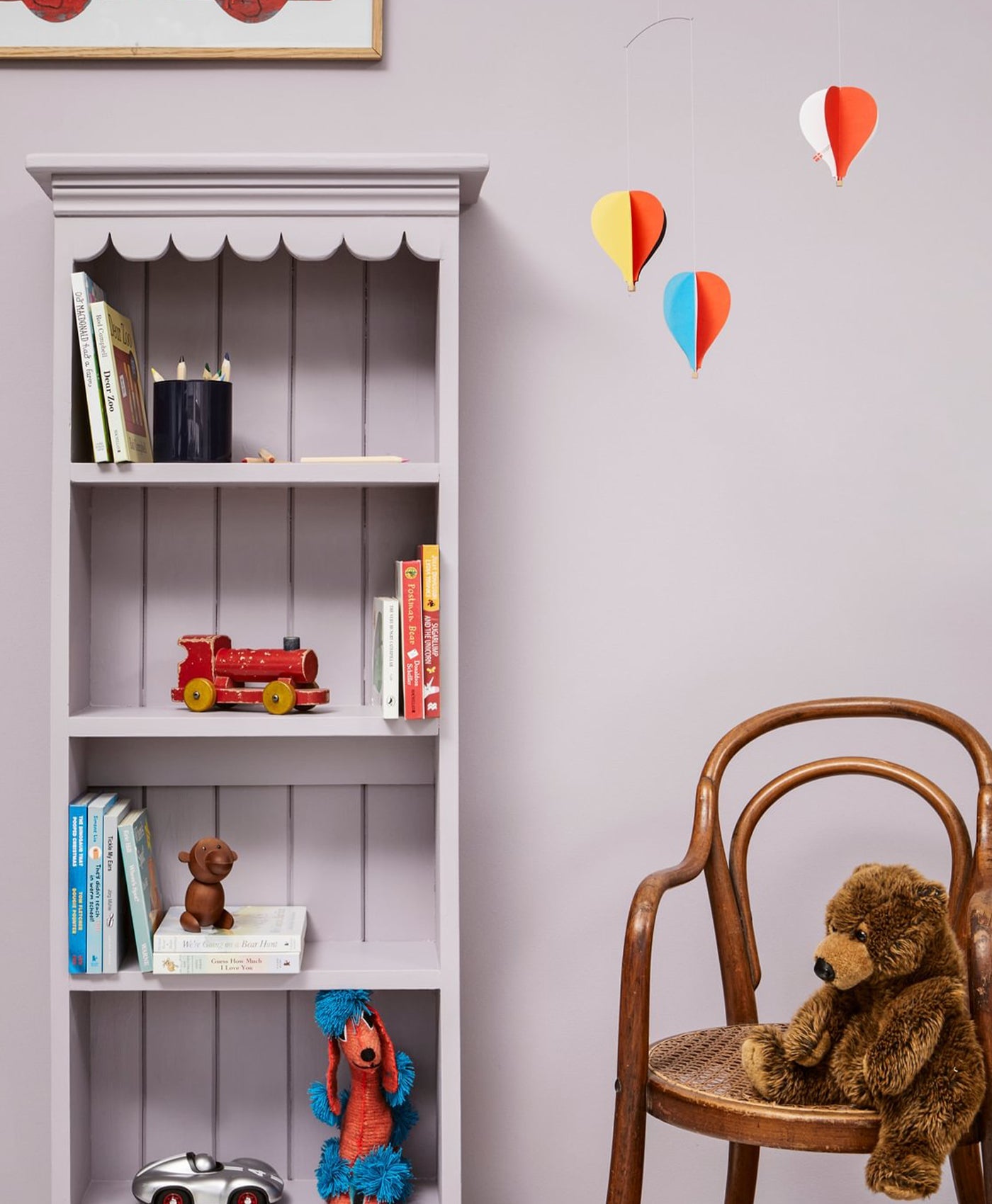 Children's room with a bookshelf, chair, and toys against a light purple wall.