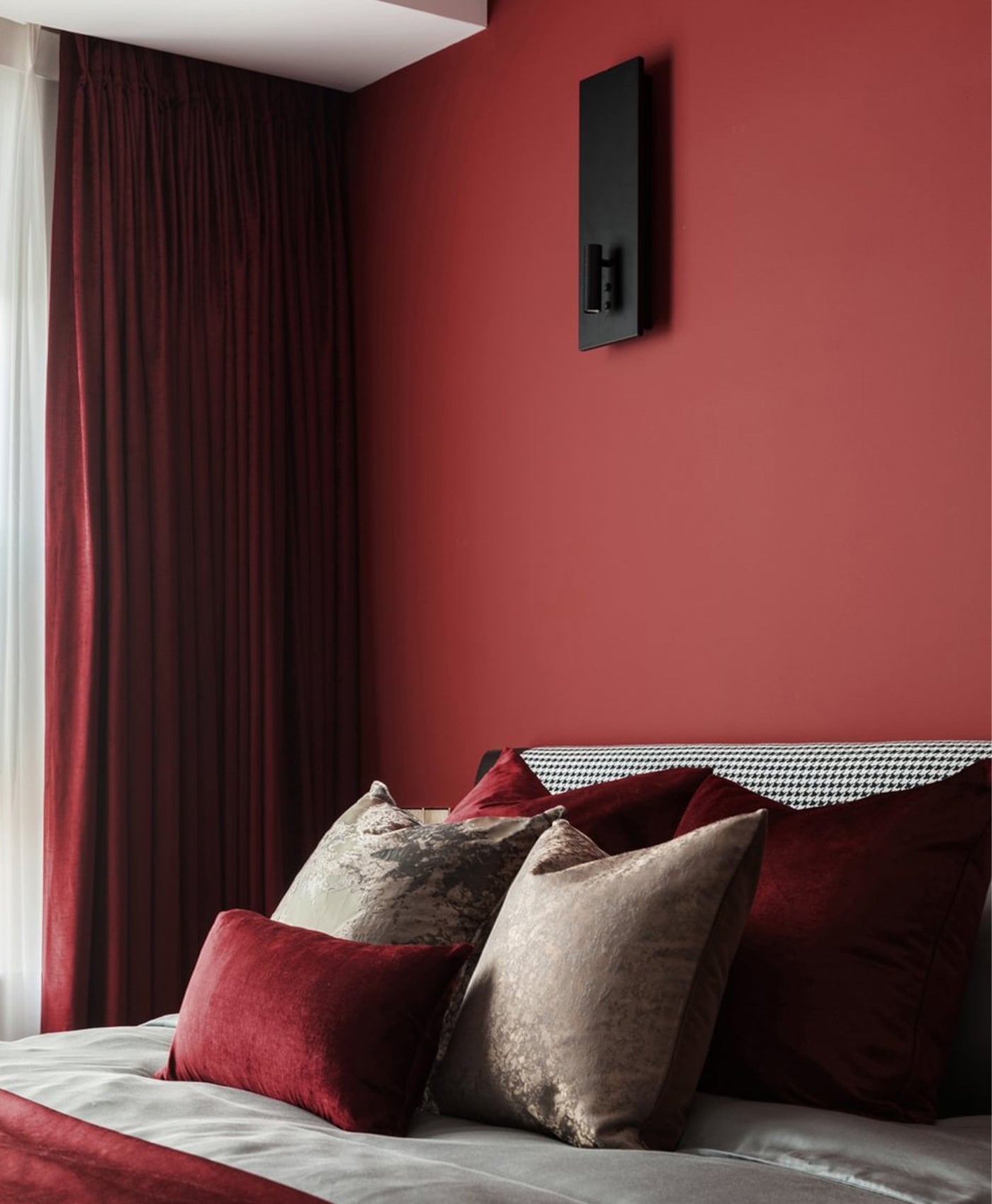 Bedroom with deep red walls, dark red curtains, and patterned pillows.