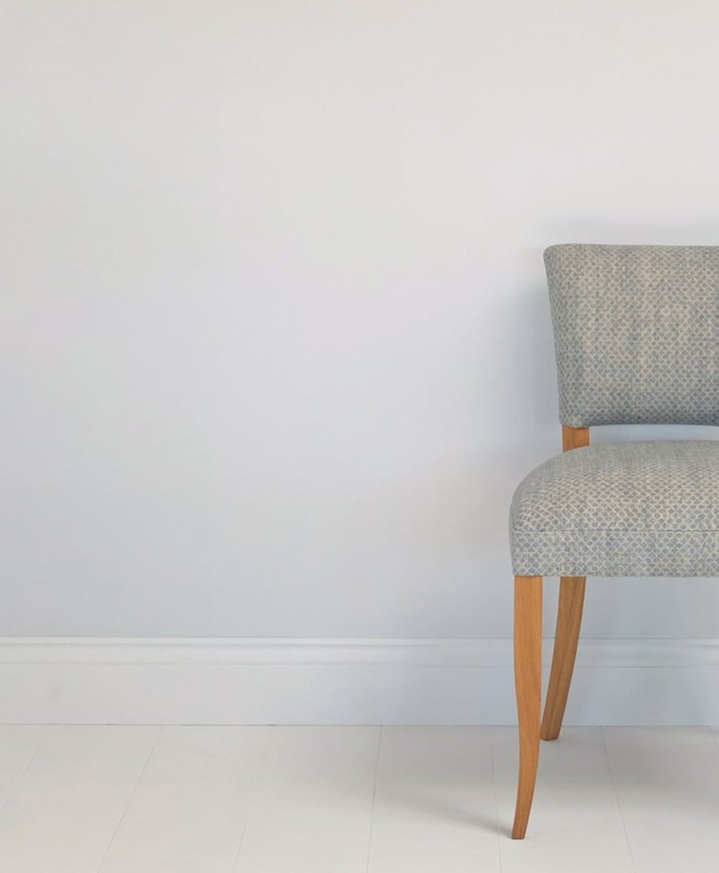 Grey upholstered chair with wooden legs against a cool white painted wall.