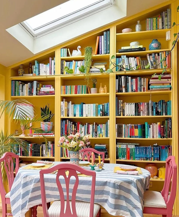 vibrant Yellow bookshelf filled with books above a dining table with pink chairs.