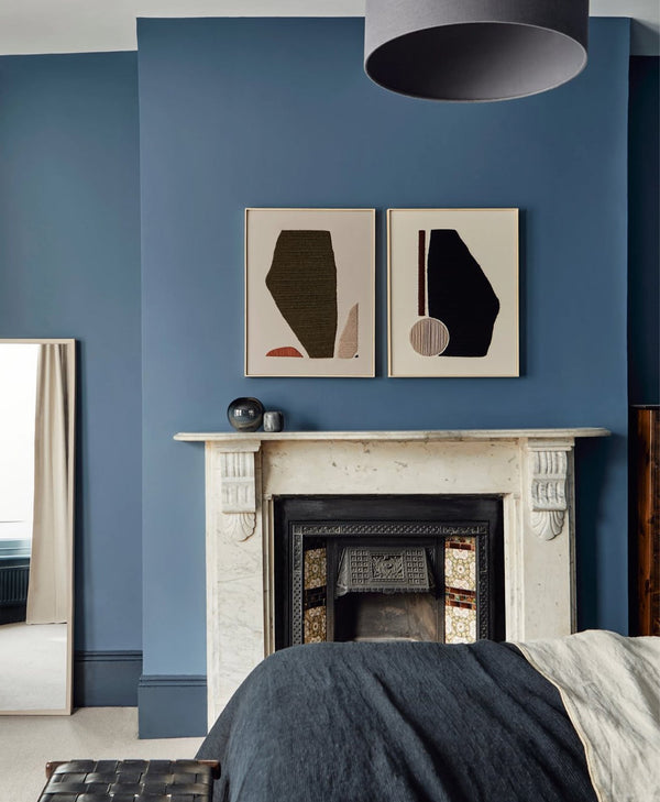 marine blue wall with abstract art above a fireplace in a bedroom.