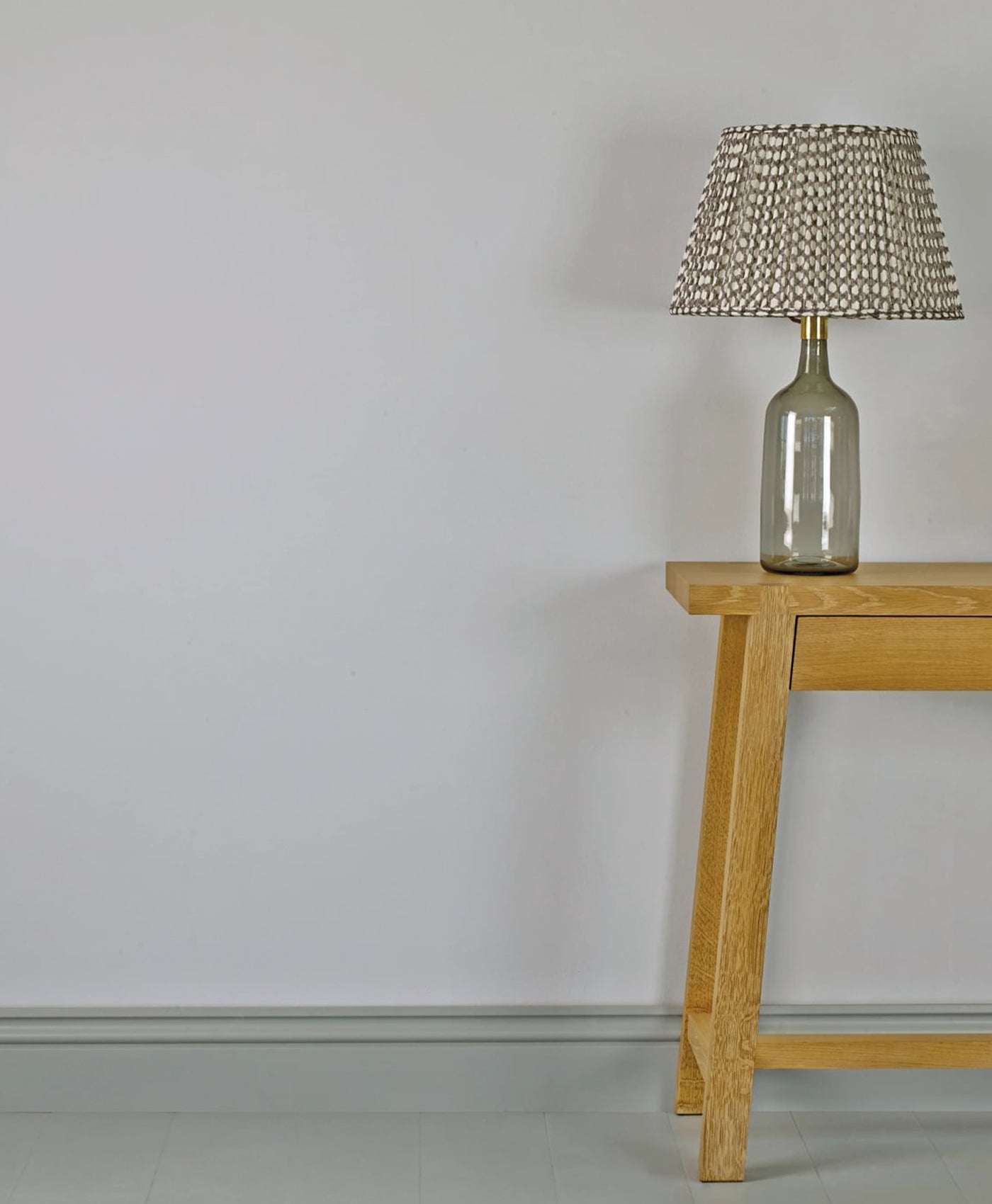 Table lamp with a textured shade on a wooden table against a pale grey wall.