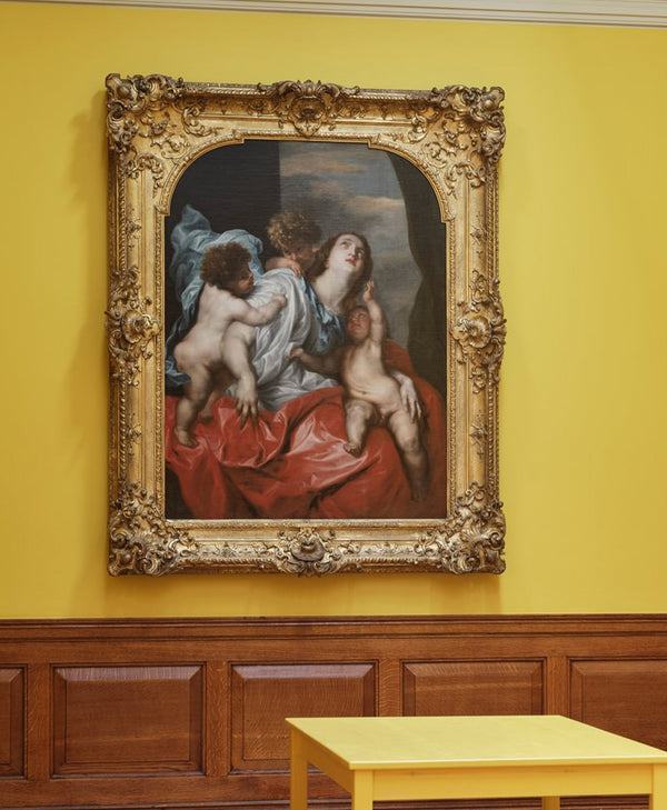 Decorative painting in an ornate gold frame on a yellow wall with wooden paneling.