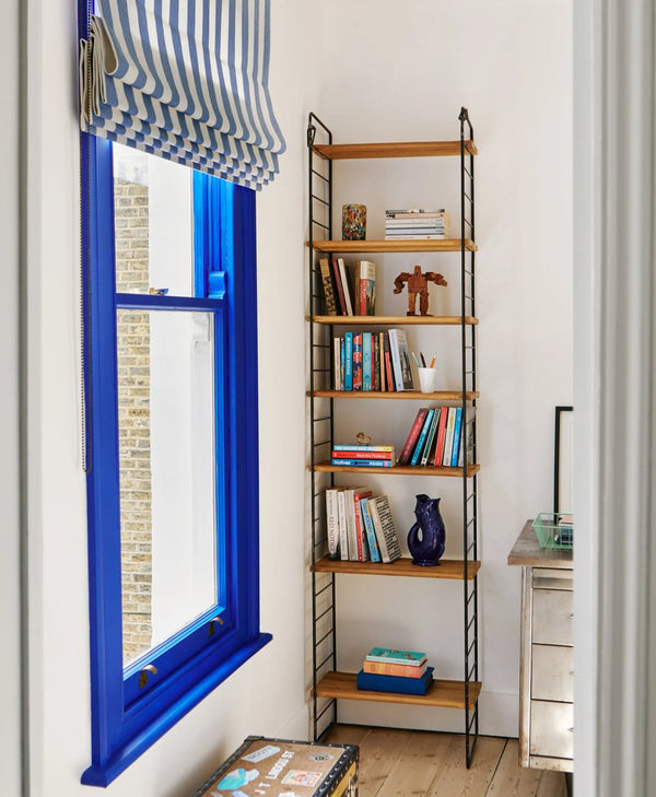 Bookshelf next to a window with blue frame and striped curtain in cool white room