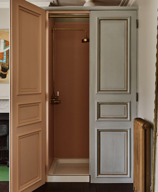 Peach bathroom with open double doors, one beige and one grey, leading to a shower area.