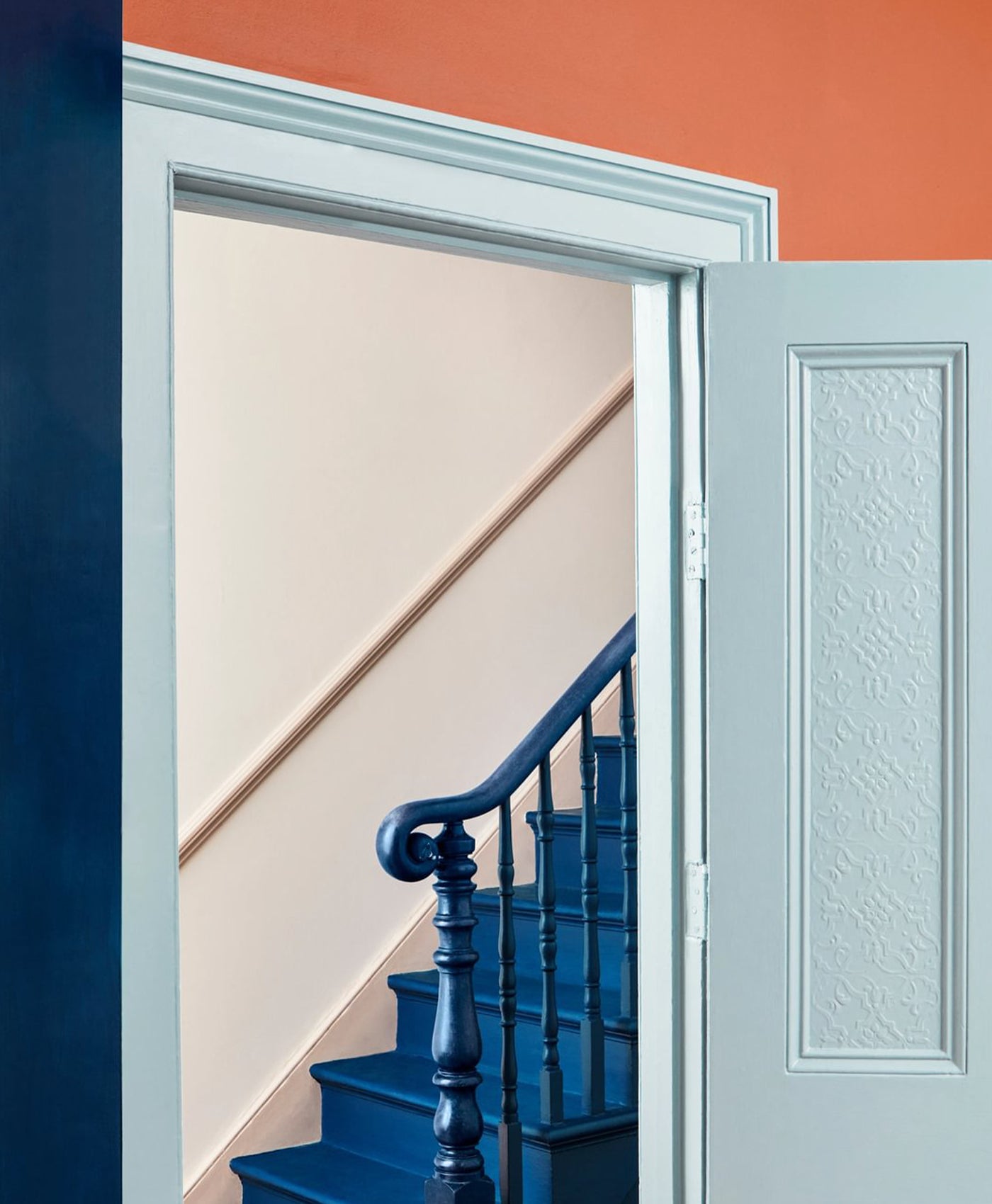 Staircase with blue railing and steps, open door leading to a room with orange wall.
