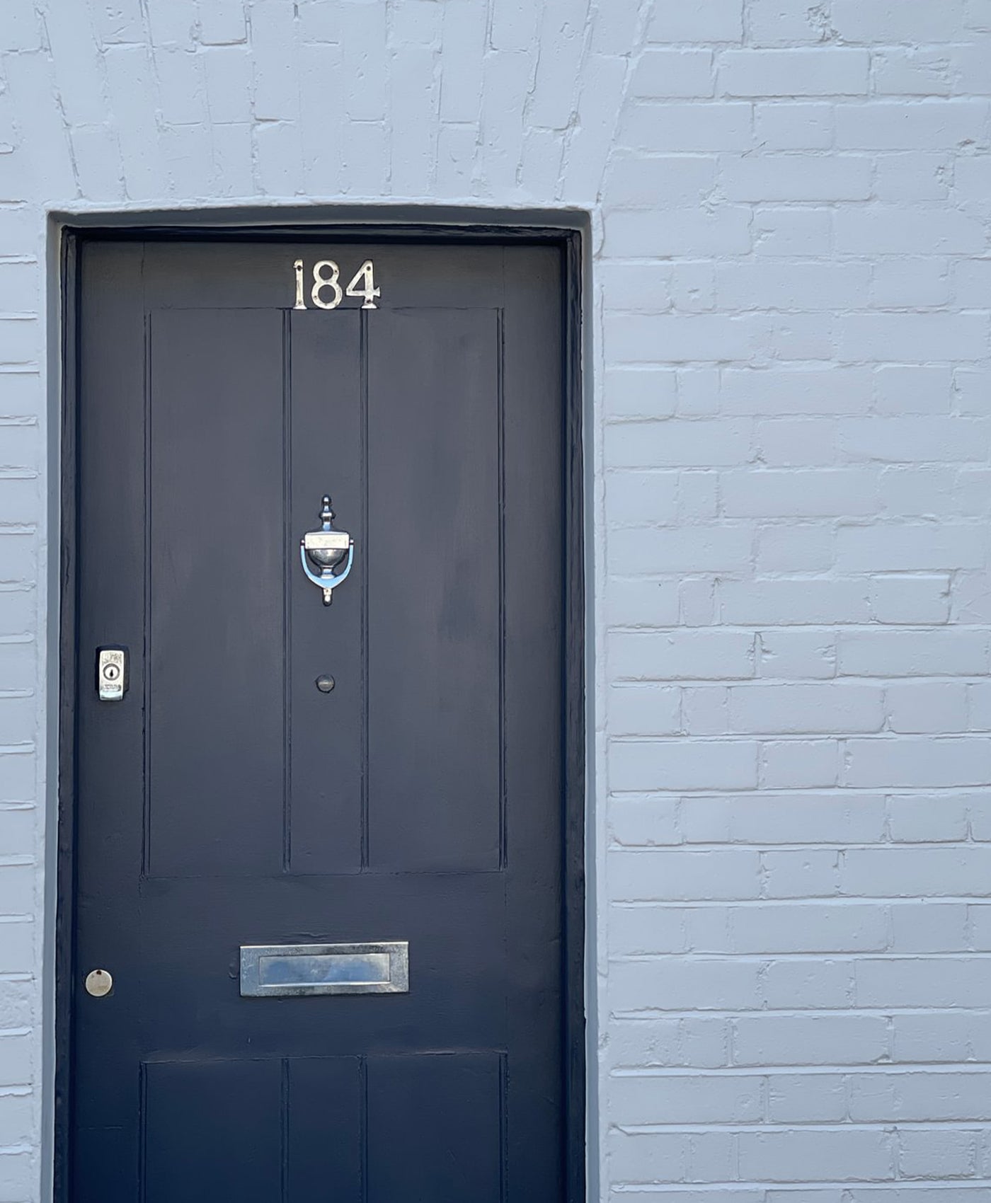 Dark blue door with the number 184 on a light grey brick wall