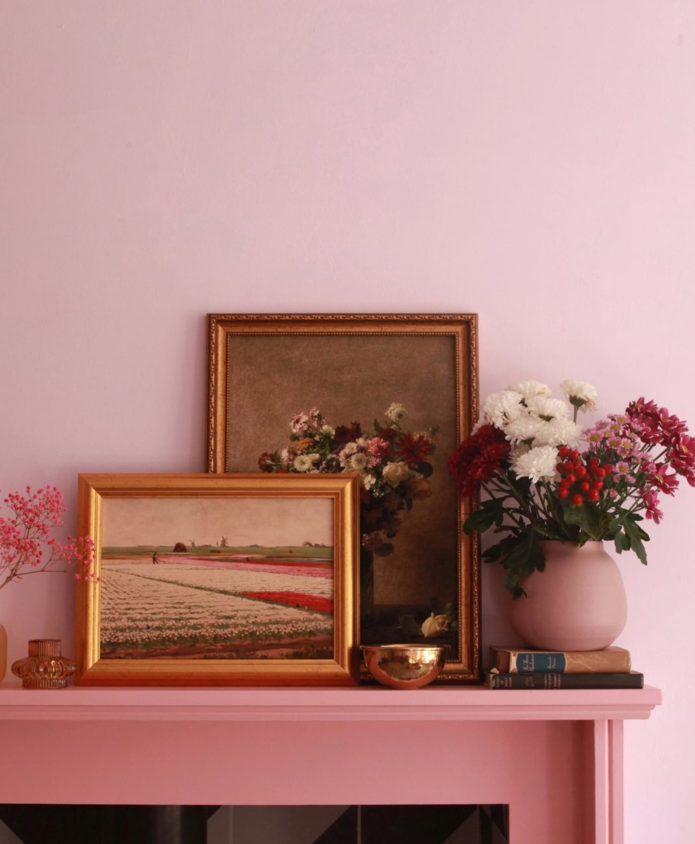 Decorative setup with framed pictures and flowers on a pink surface against a blush pink wall.