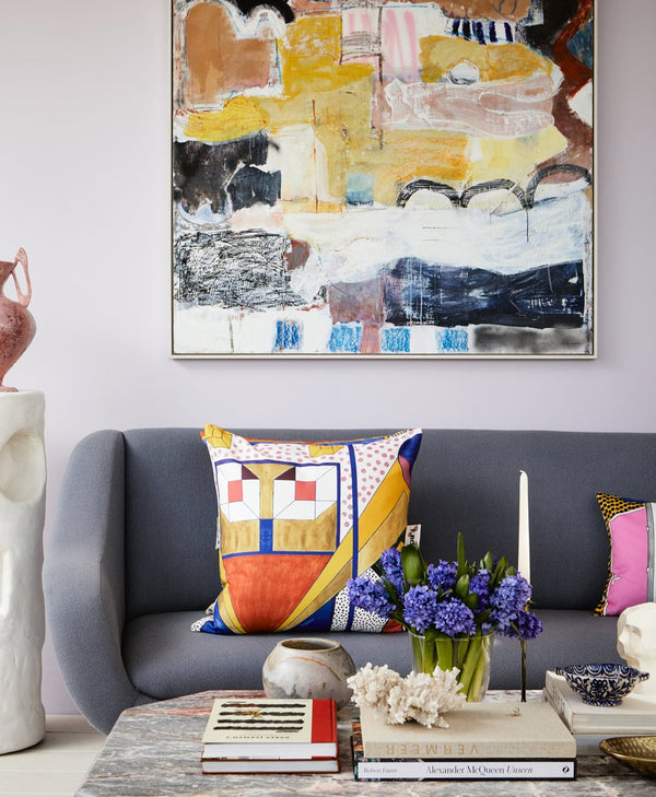 Lavender living room with a gra=ey sofa, colourful pillows, and abstract art on the wall.