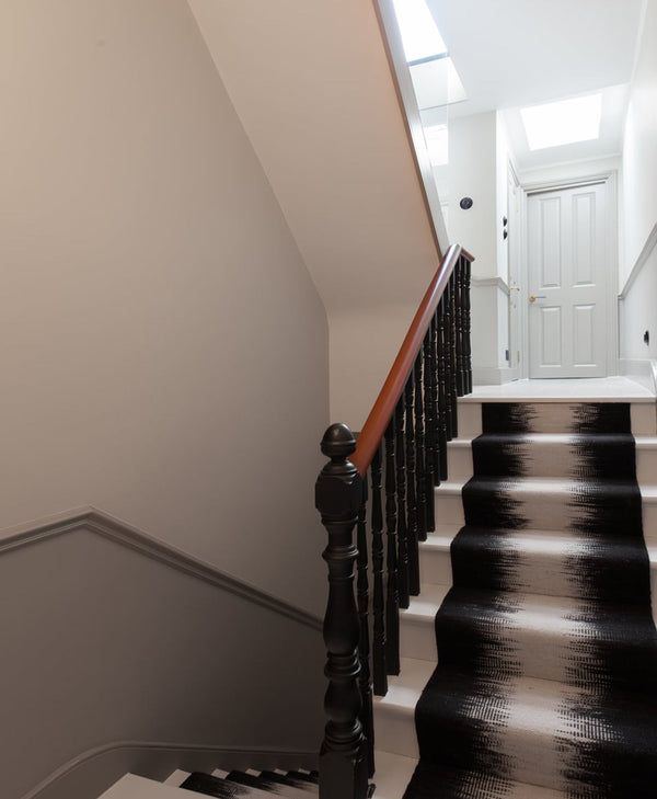 Staircase with wooden handrail and black balusters leading to a white door.