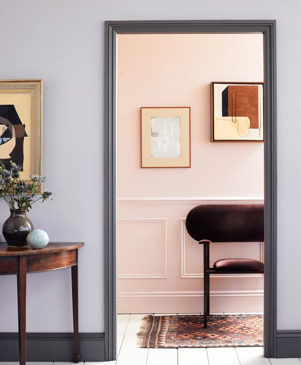 Lilac grey room with dark grey skirting leading to light pink room and wooden panelling and dark red velvet chair