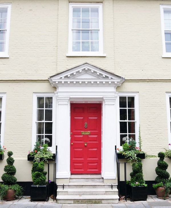 Red door with traditional white paint surround, on a light-coloured building with decorative elements