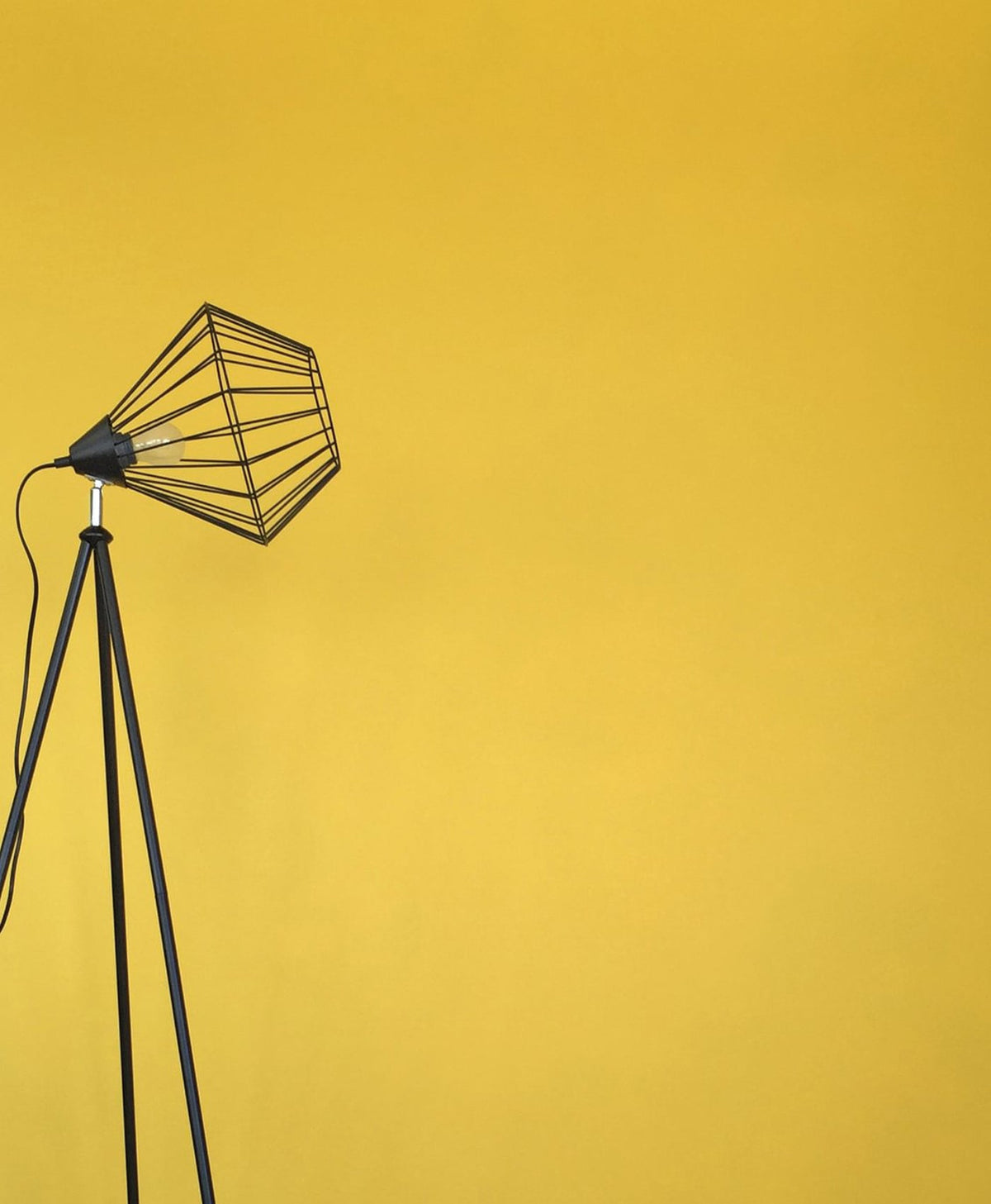 Black floor lamp with wire cage shade on a yellow background