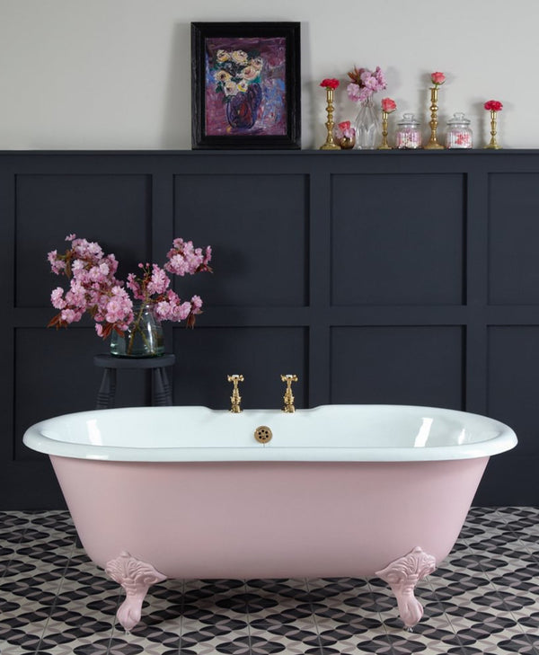 Pink freestanding bathtub in a bathroom with dark paneling and decorative elements.