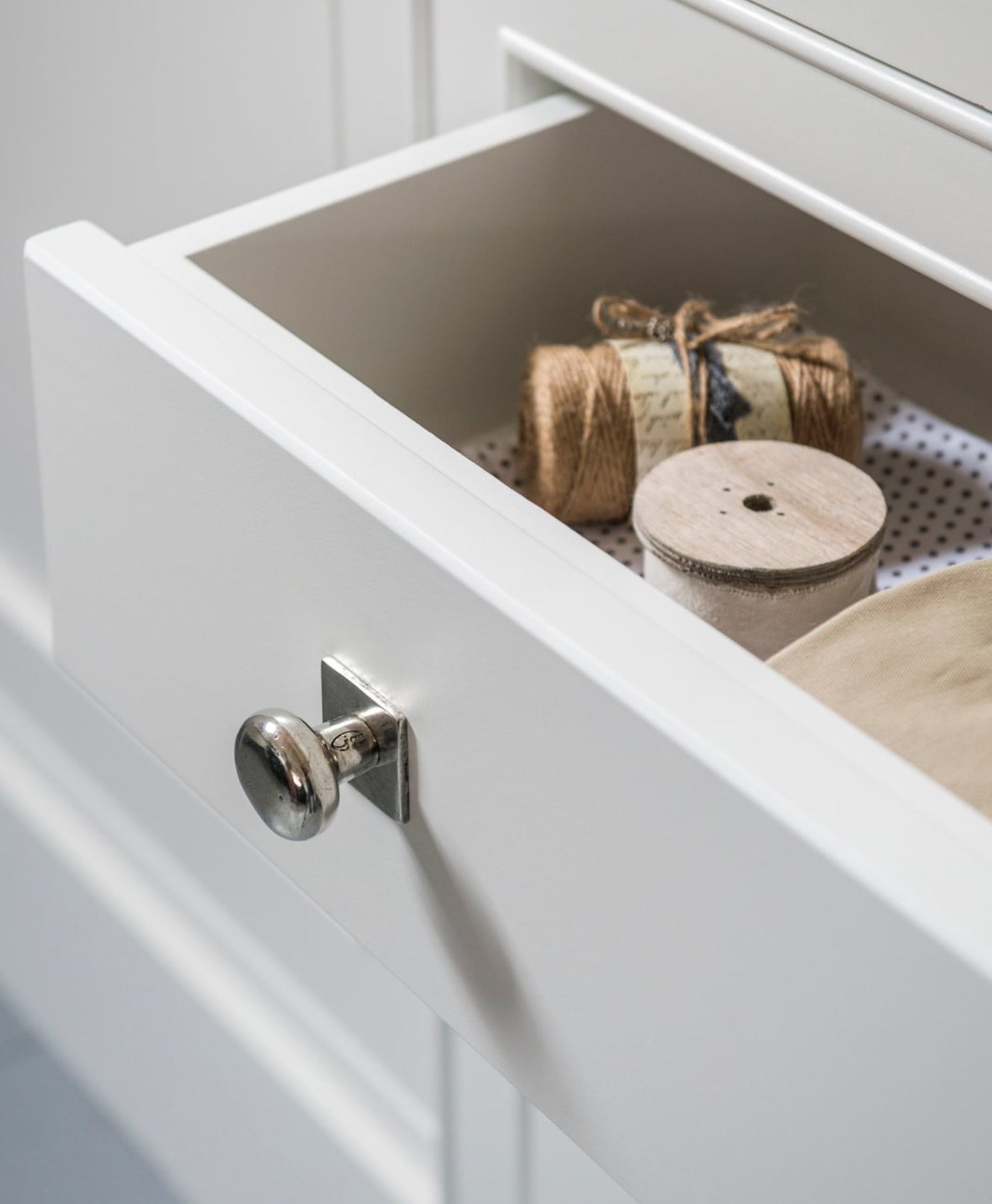 Open white drawer with spools of twine and a wooden spool inside.