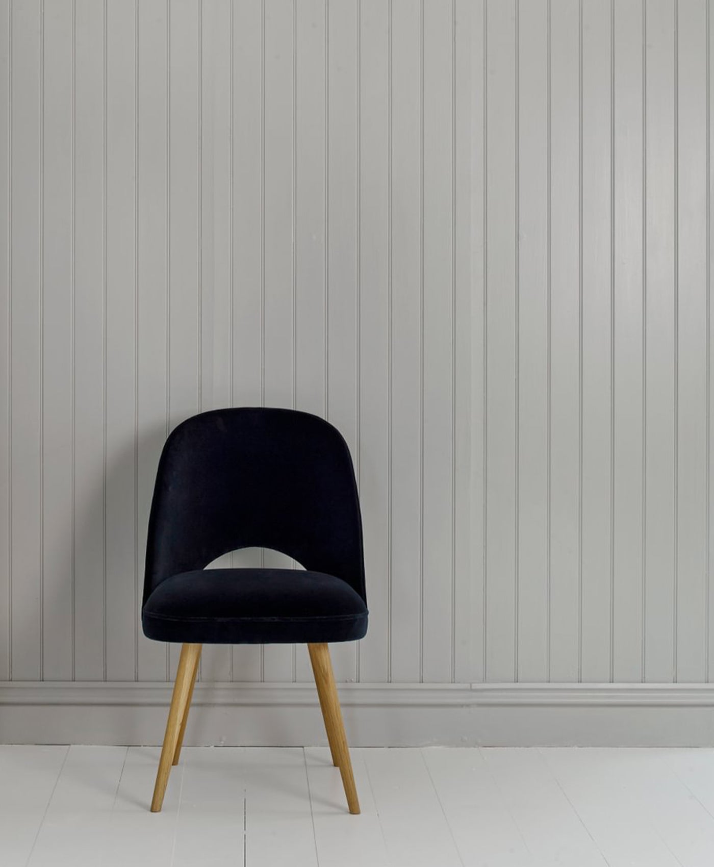 Black velvet chair with wooden legs against a grey panelled wall.