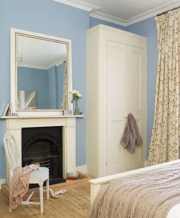 Grey blue room interior with a fireplace, mirror, wardrobe, and bed.