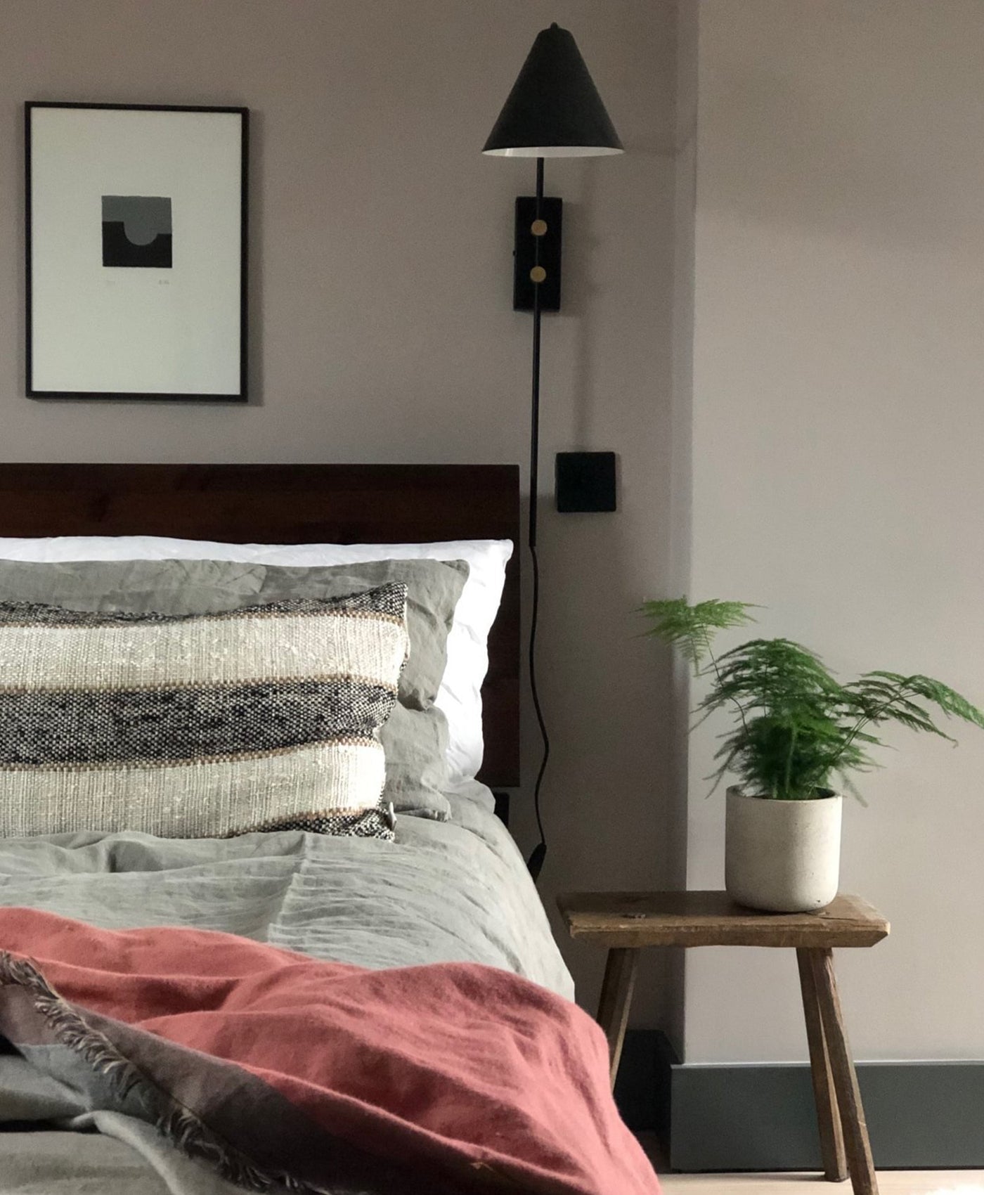 Cosy warm grey bedroom with a bed, nightstand, and wall lamp.